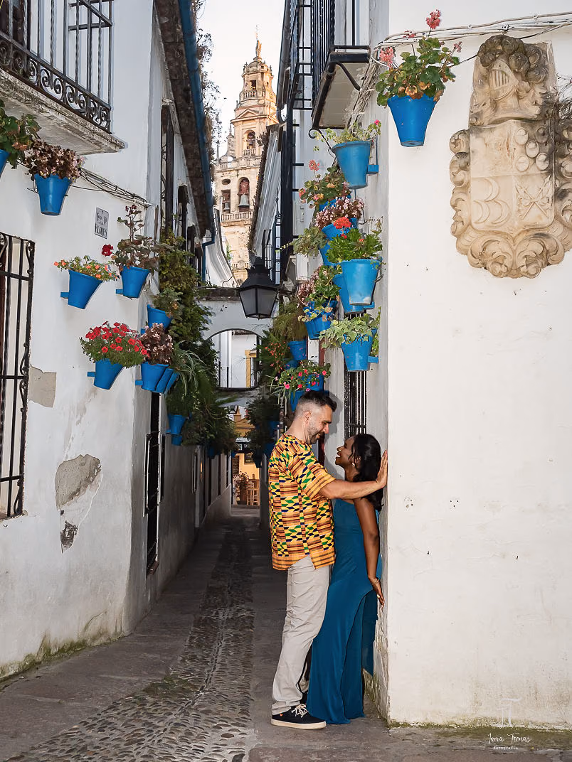 Pablo and Seraphine in a narrow whitewashed alley of the Jewish Quarter, blue flowerpots on the walls and the Mezquita's bell tower at the end of the street.
