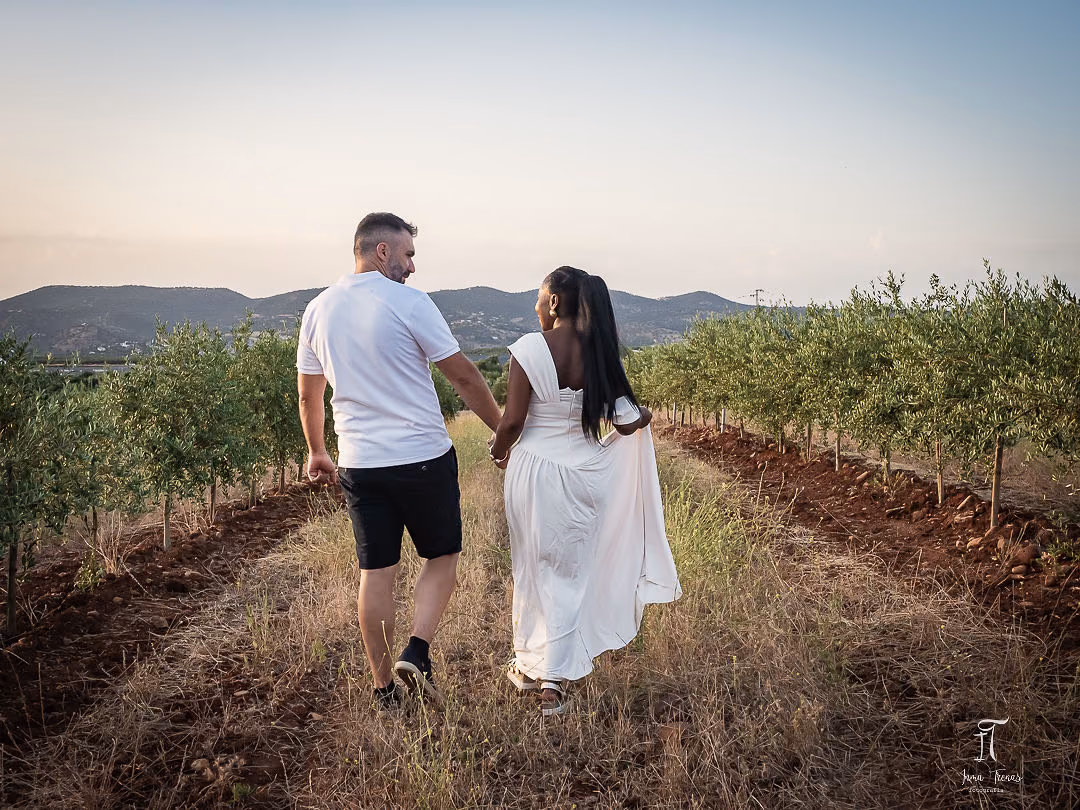 Pablo and Seraphine walking hand in hand away down a row of young olive trees at dusk.