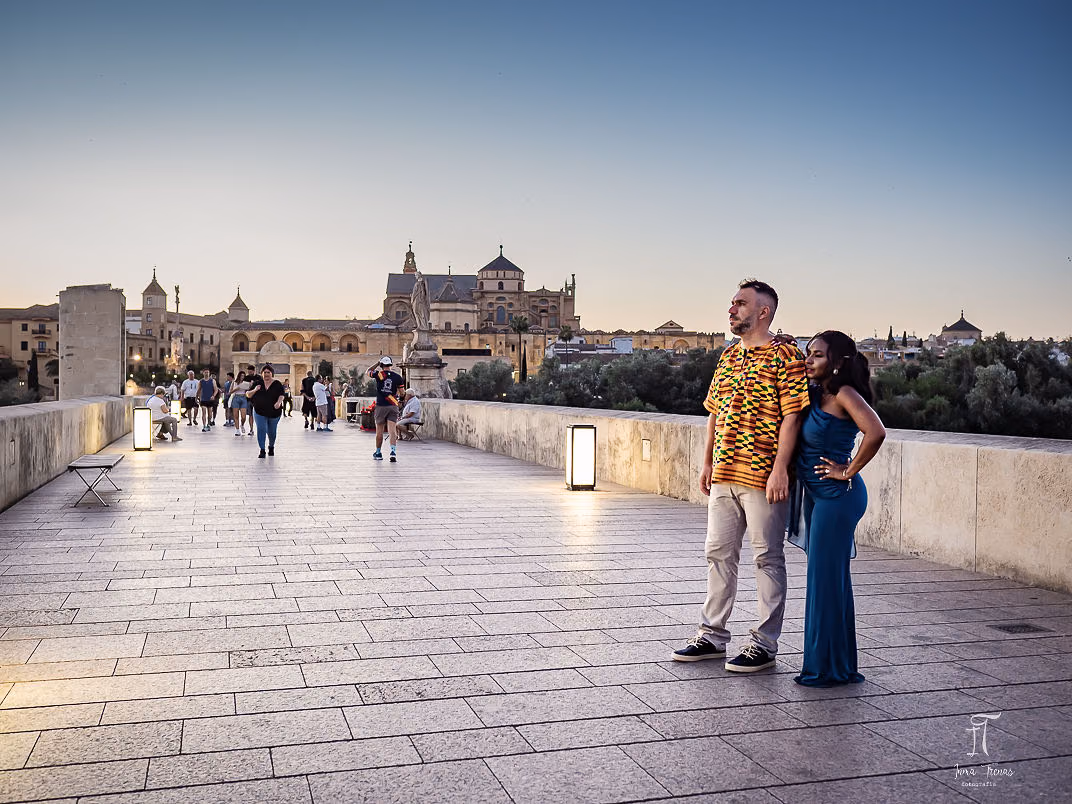 Pablo and Seraphine on the Roman Bridge at dusk, the lit Mezquita and the old city behind them.